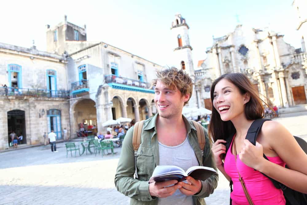 A couple is traveling while smiling and looking at a map in a bright European city.