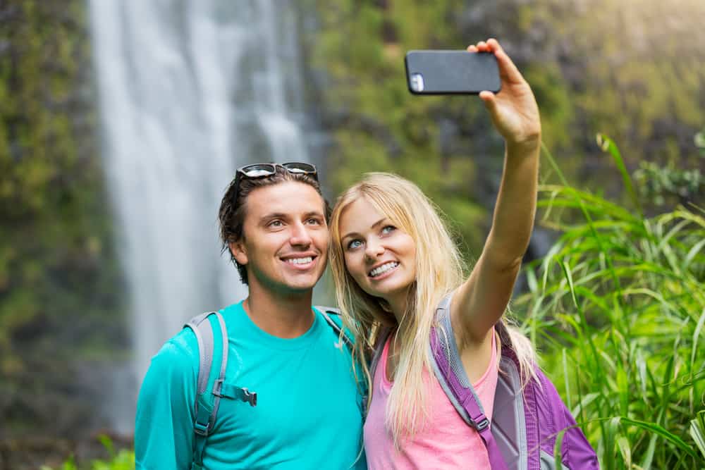 A couple takes a selfie with a camera phone next to a waterfall.