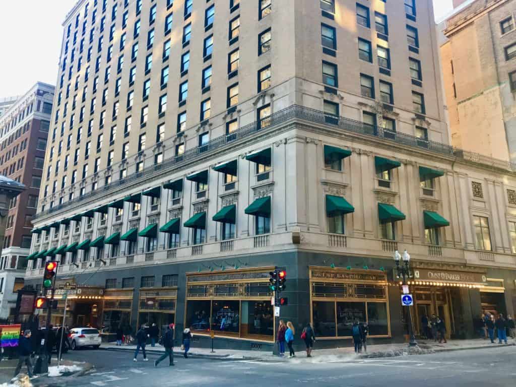 Big sandy colored hotel with green awnings on a street corner.