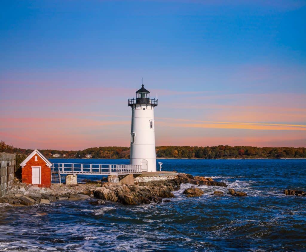 A white lighthouse is on an island surrounded by water under a sunset sky.