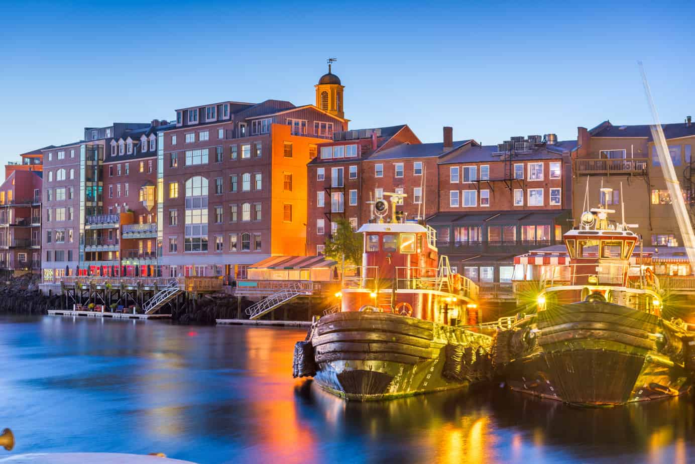 Colorful buildings and a large boat reflecting into a body of water in Portsmouth New Hampshire