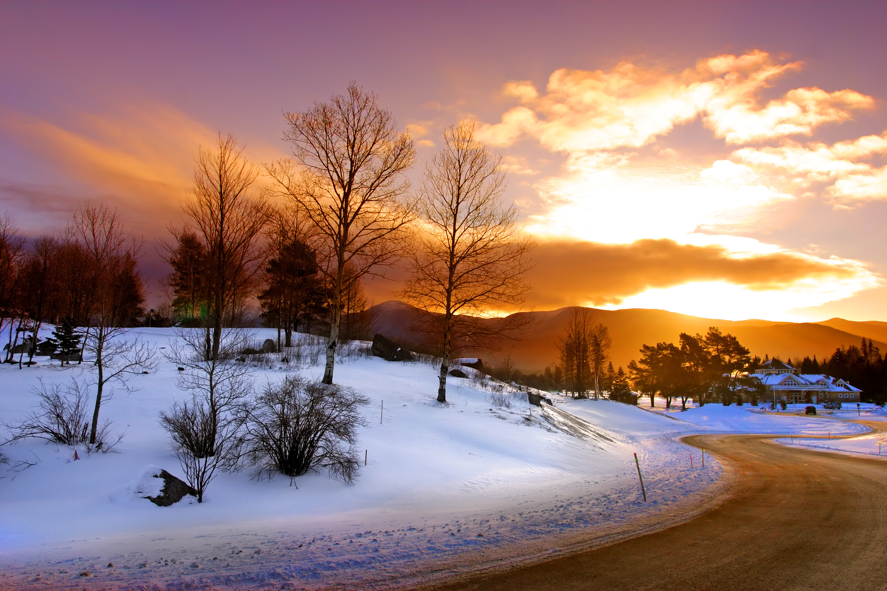A sunset with purple and orange colors over a snowy street. Mountains are in the background.