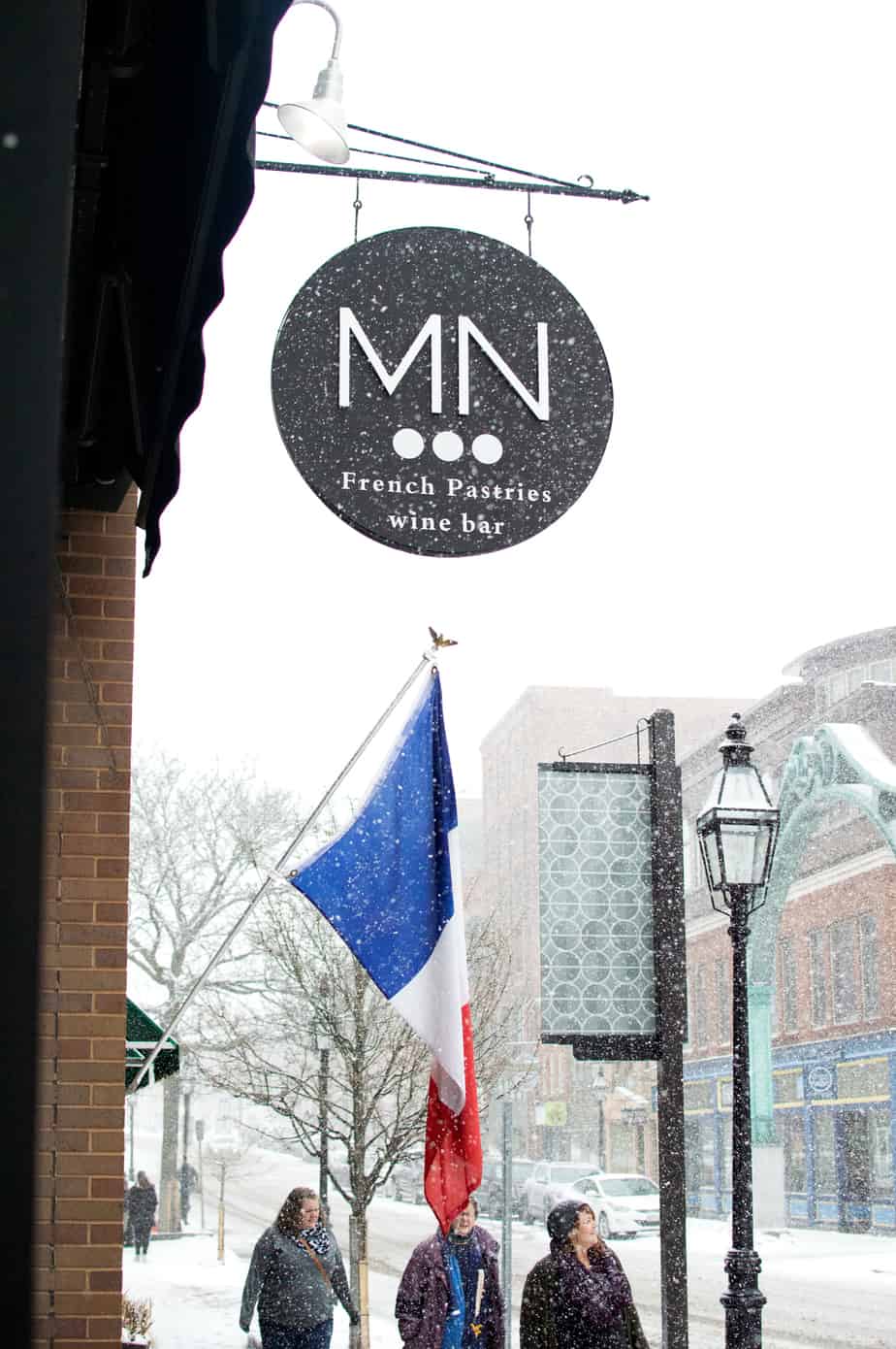 People walking down the sidewalk in the snow past a wine bar
