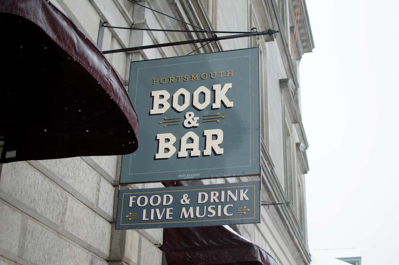 A street sign sitting on the front of a building that reads \"Book & Bar\"