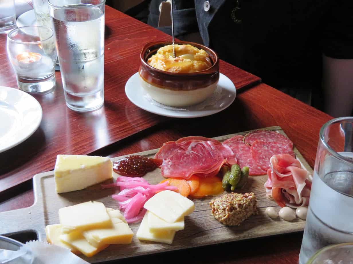 A platter of cheese and meat and a bowl of food and glass of water on a table