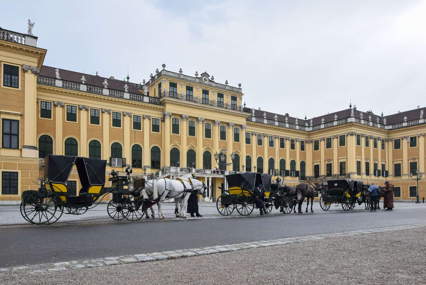 Horse-drawn carriages in front of a yellow palace.