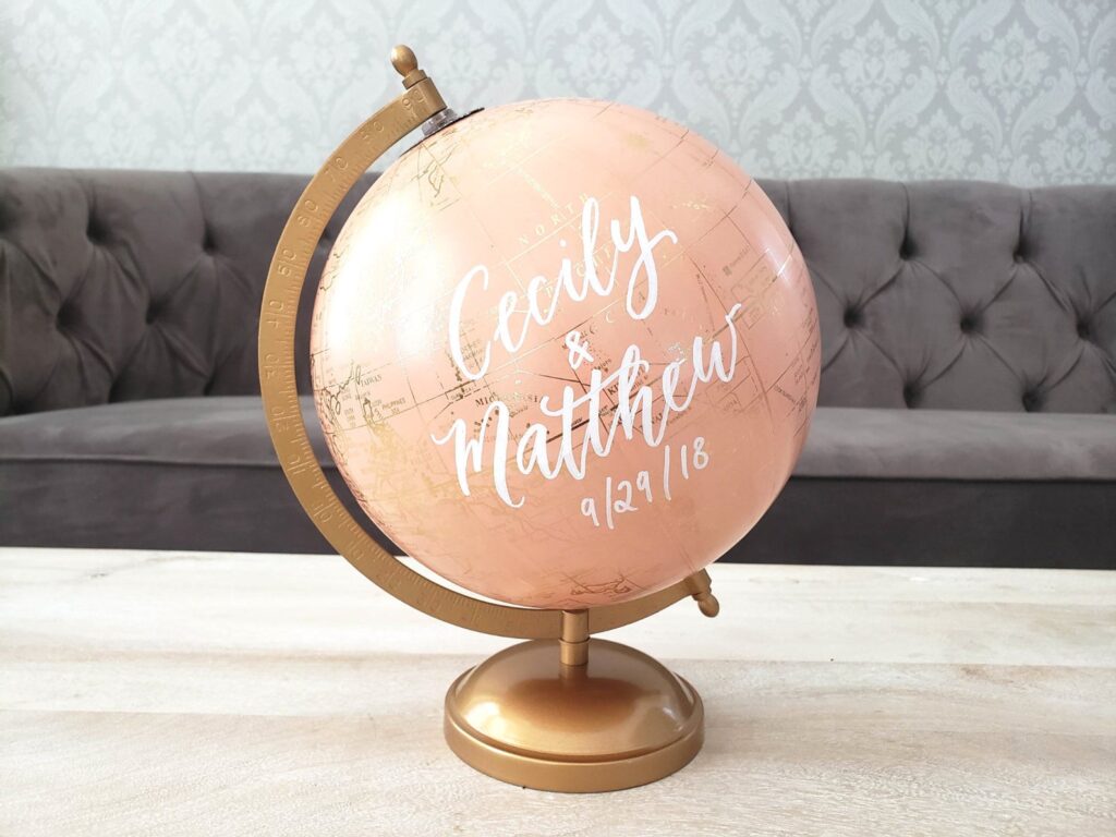 A pink globe with gold detailing that says \"Cecily & Matthew. 9/29/18.\"