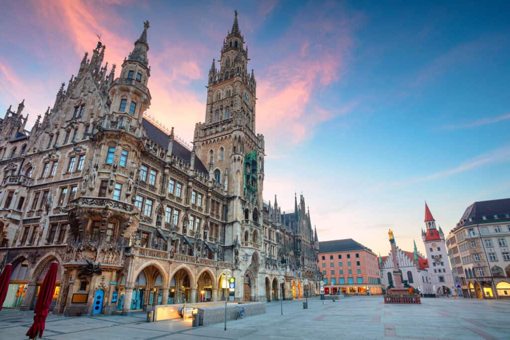 An empty plaza in front of a tall historic building under a pink and blue sky.