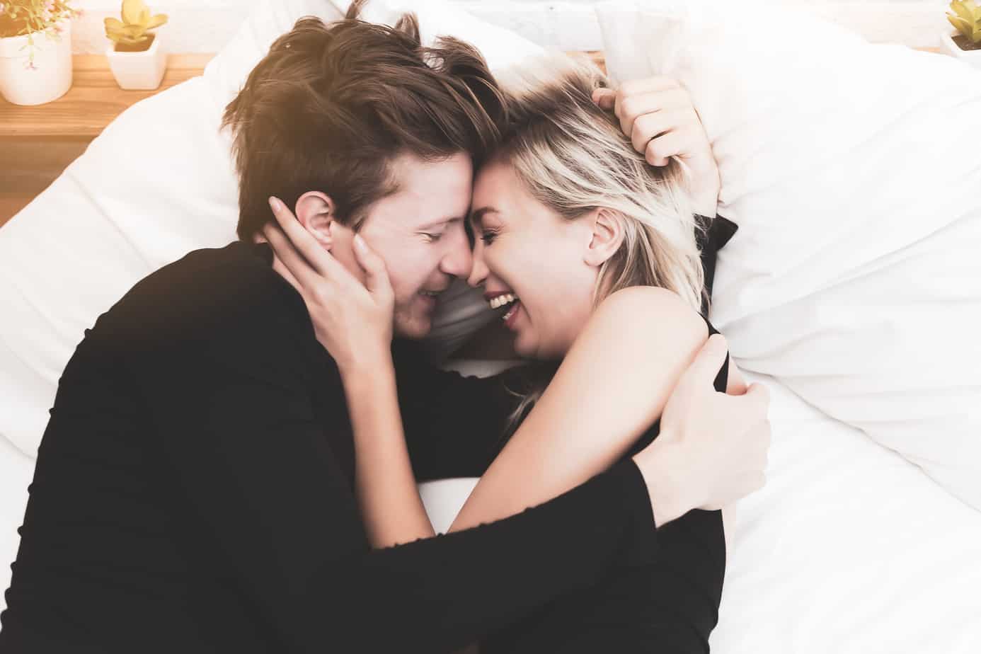 header for reasons why i love you list - attractive couple laughing and cuddling in bed white sheets