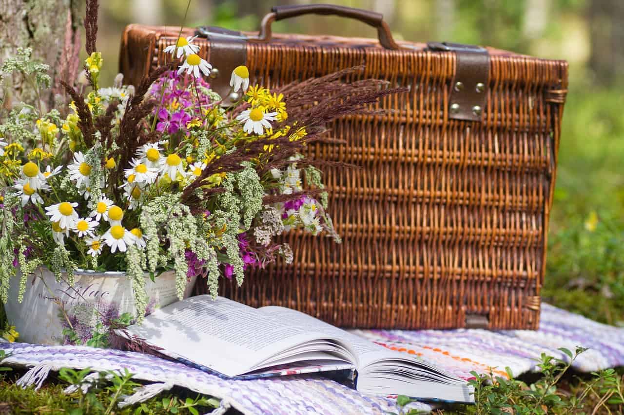 Close up of a brown picnic basket with flowers and a book sitting next to it.