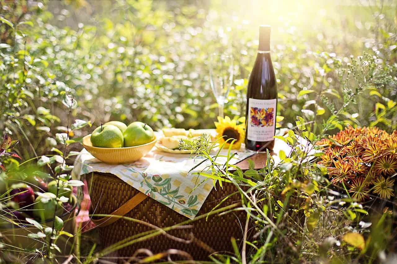 A picnic basket has apples and wine on top.