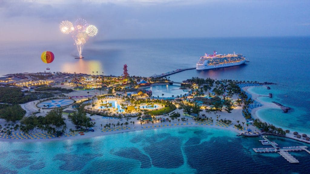 Aerial view of an island surrounded by blue water. A cruise ship floats behind.