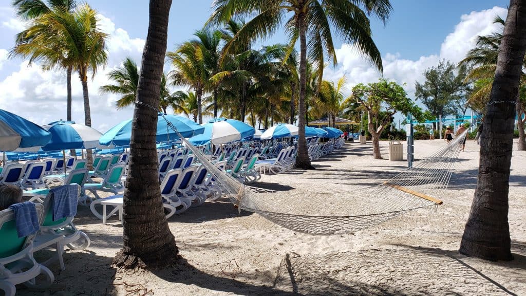 An empty hammock on the beach surrounded by palm trees.