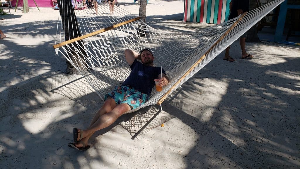 A man smiling and laying in a hammock on the beach.