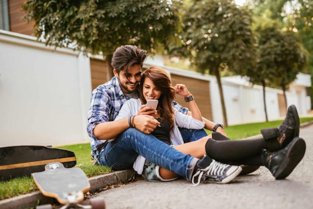 A couple sits outside while reading a message on the same phone.