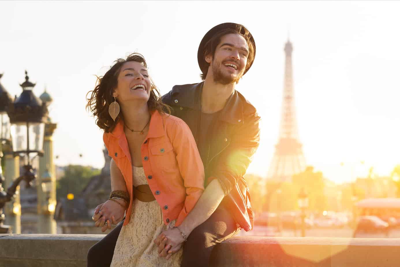 A couple smiles outdoors with the Eiffel Tower behind them.