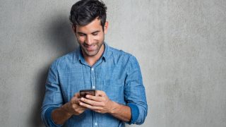 A man smiles while reading a text message on his phone.