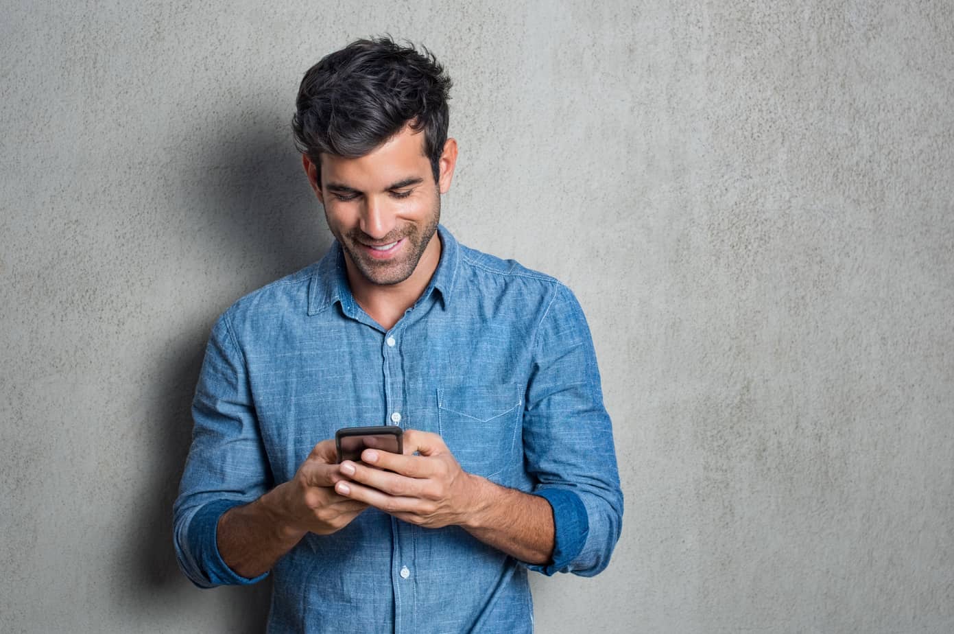 A man smiles while reading a text message on his phone.