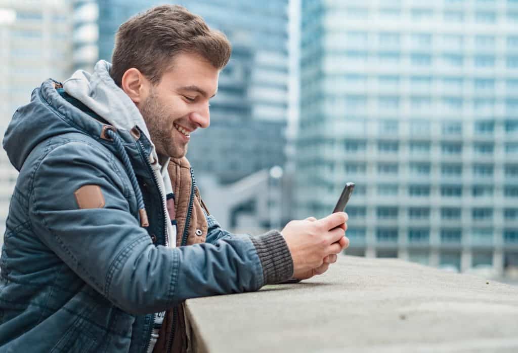 A man smiles while reading a message on his phone.