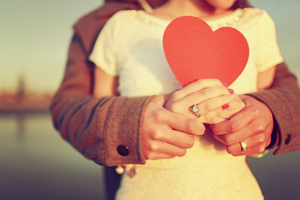 A couple holds each other while the woman holds a red heart.