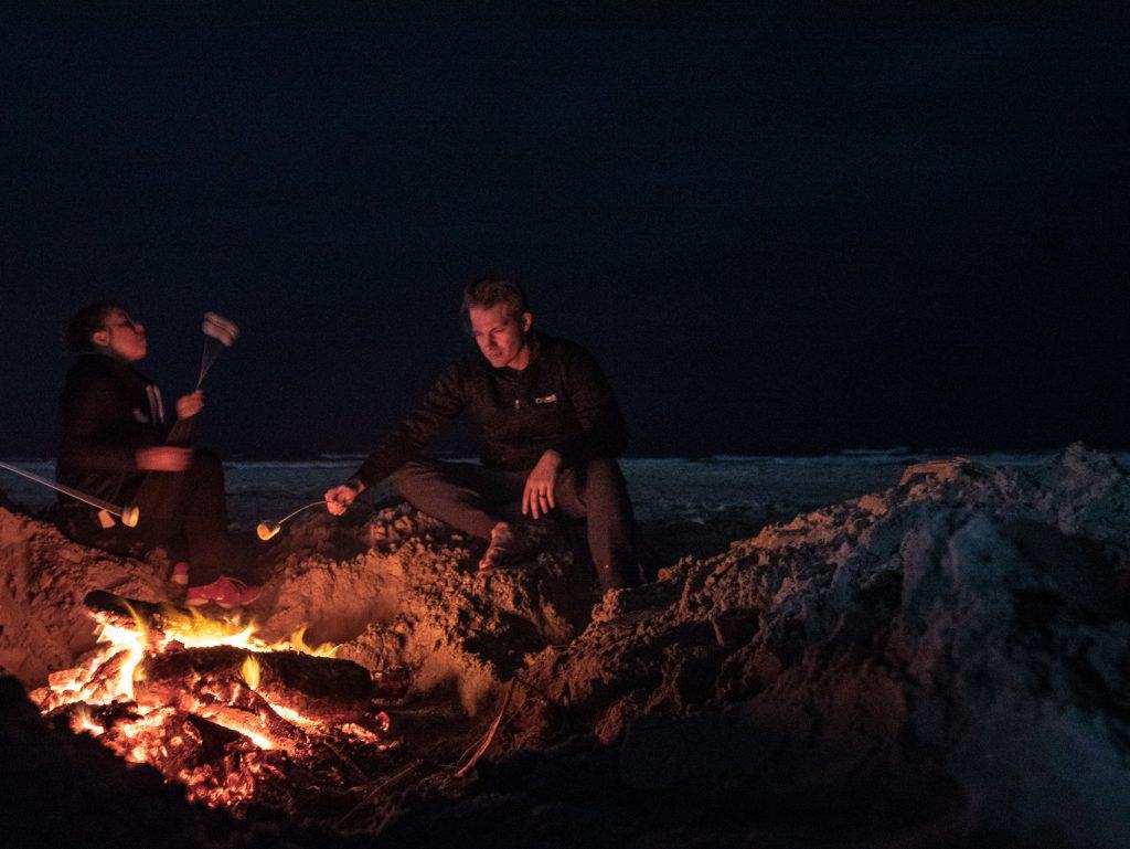 People roast marshmallows by a fire on the beach.