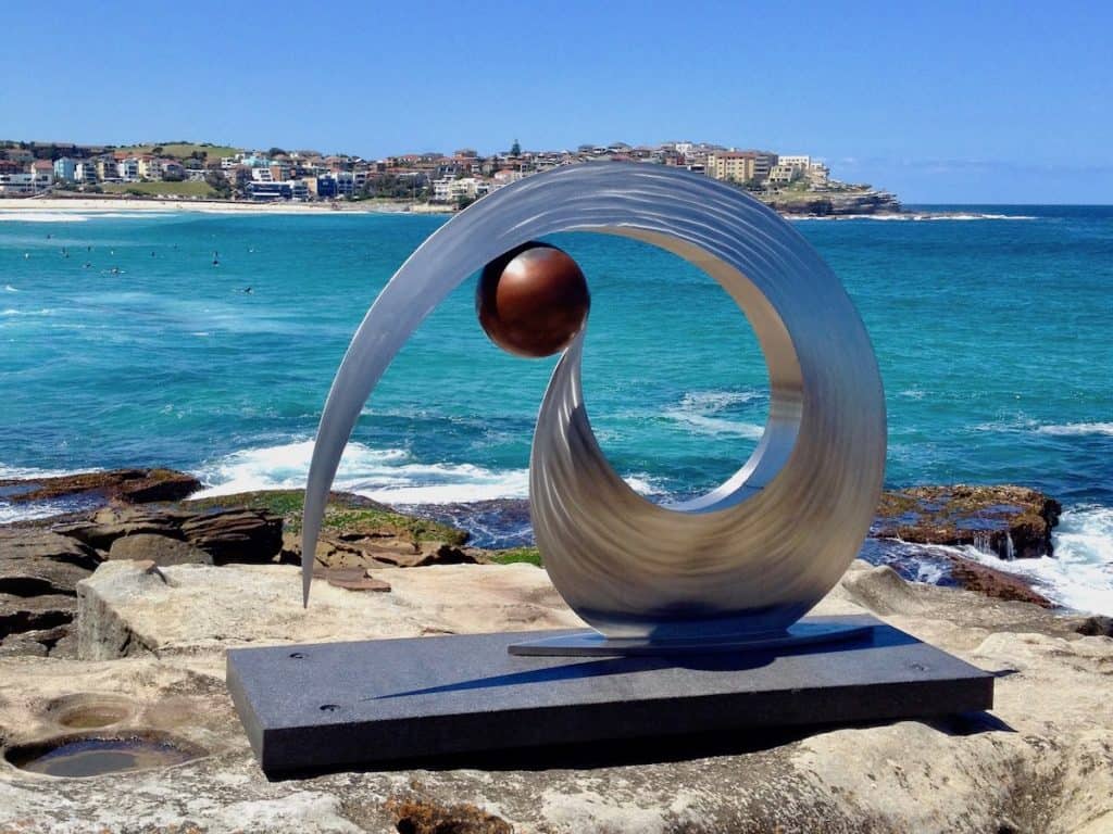 A sculpture stands on a rock next to the blue ocean.