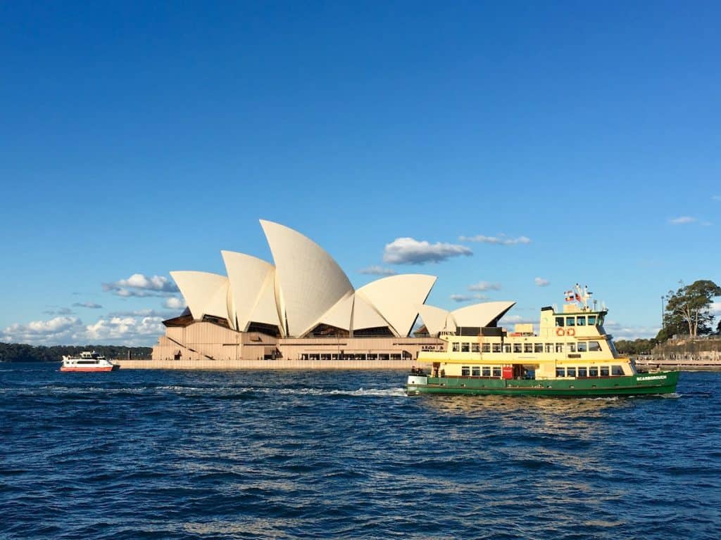 A boat floats on the water by the famous Sydney Opera House.