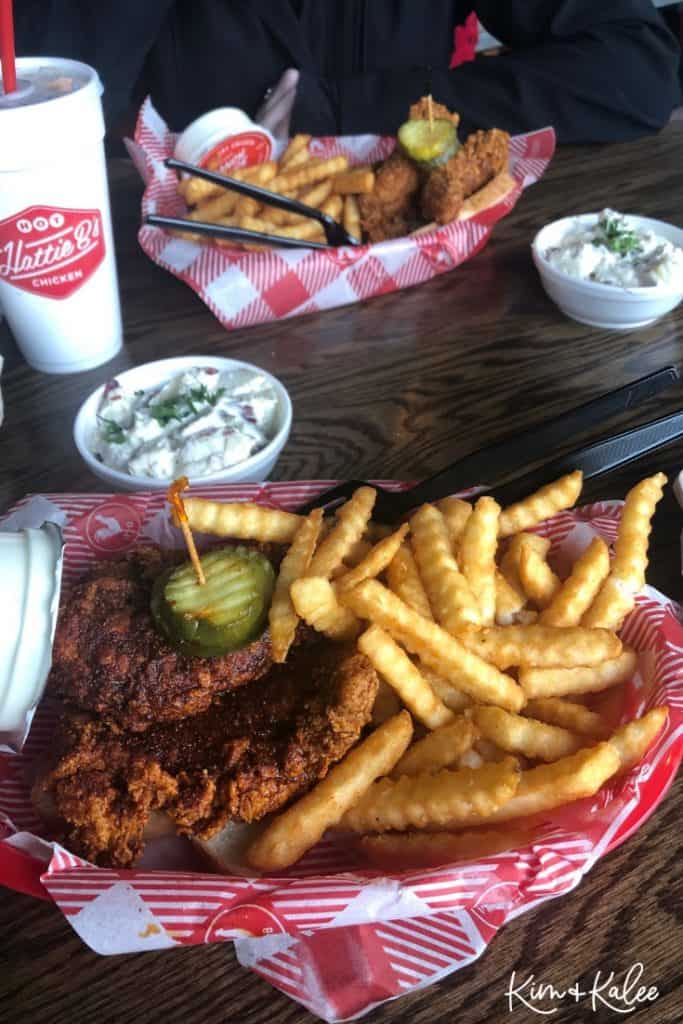 Food on a red plate that features french fries, chicken, and a pickle.