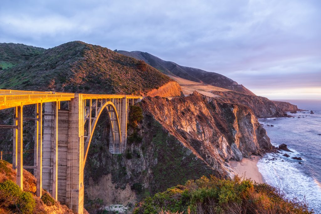 A big bridge goes over a cliff near the water.