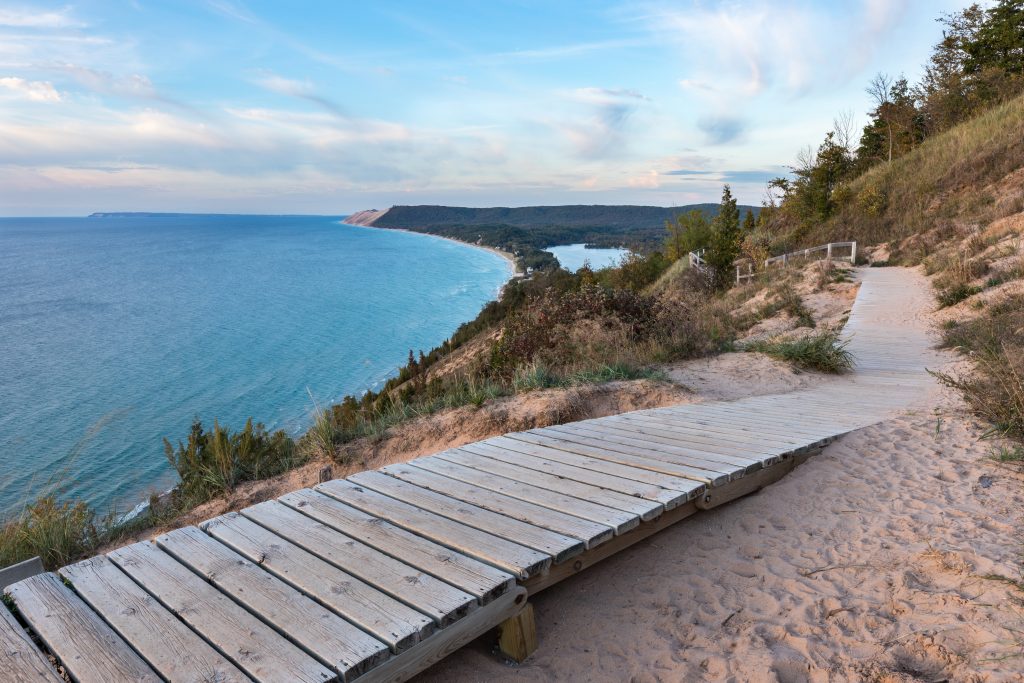 A weathered wooden walkway is empty and goes around a beach landscape.
