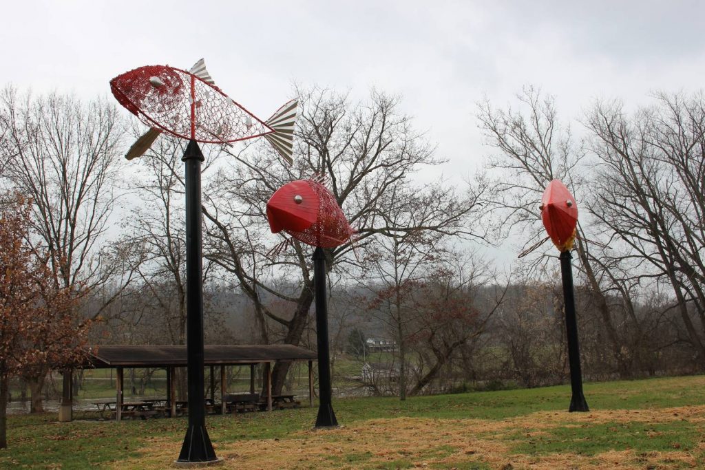 Large red fish statues stand in a field.