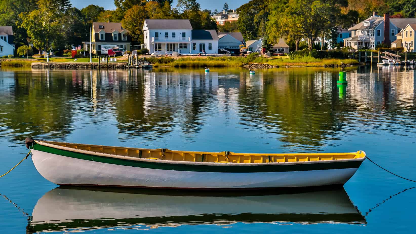 White and green boat floating on a lake with houses along the lakeside.