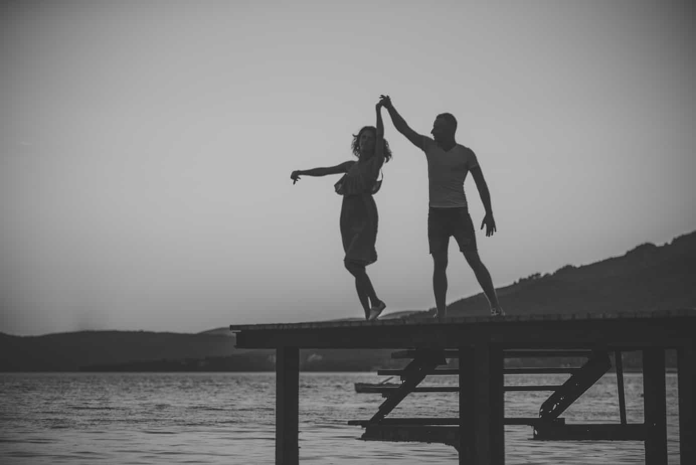 A couple twirls and dances together on a pier by the water.