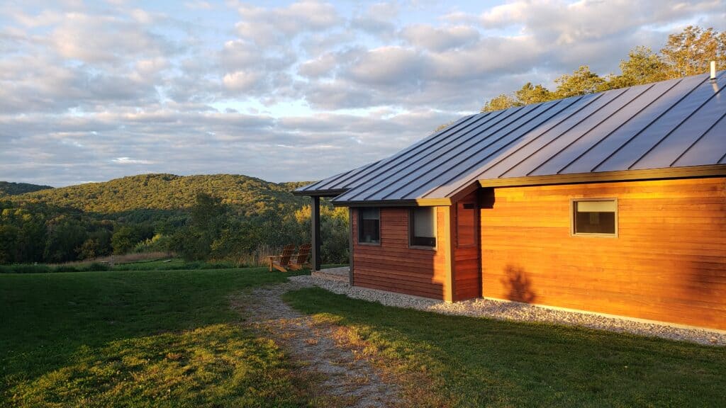 Wooden modern house with a black roof half-covered in sunshine. The sky is blue and cloudy.