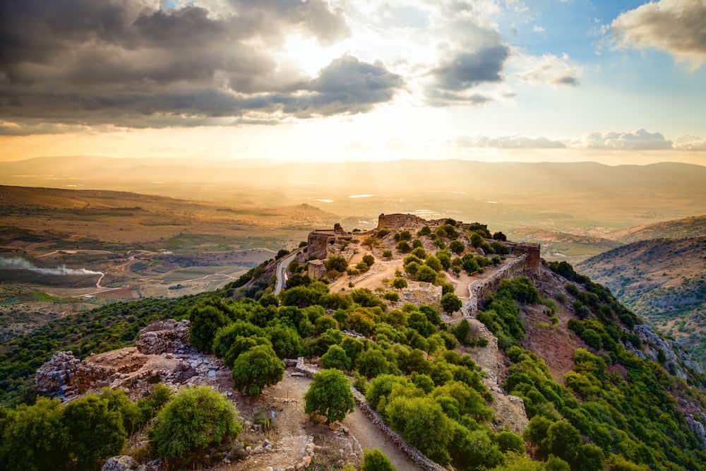 View of ruins on top of a mountain as the sun sets in the distance.