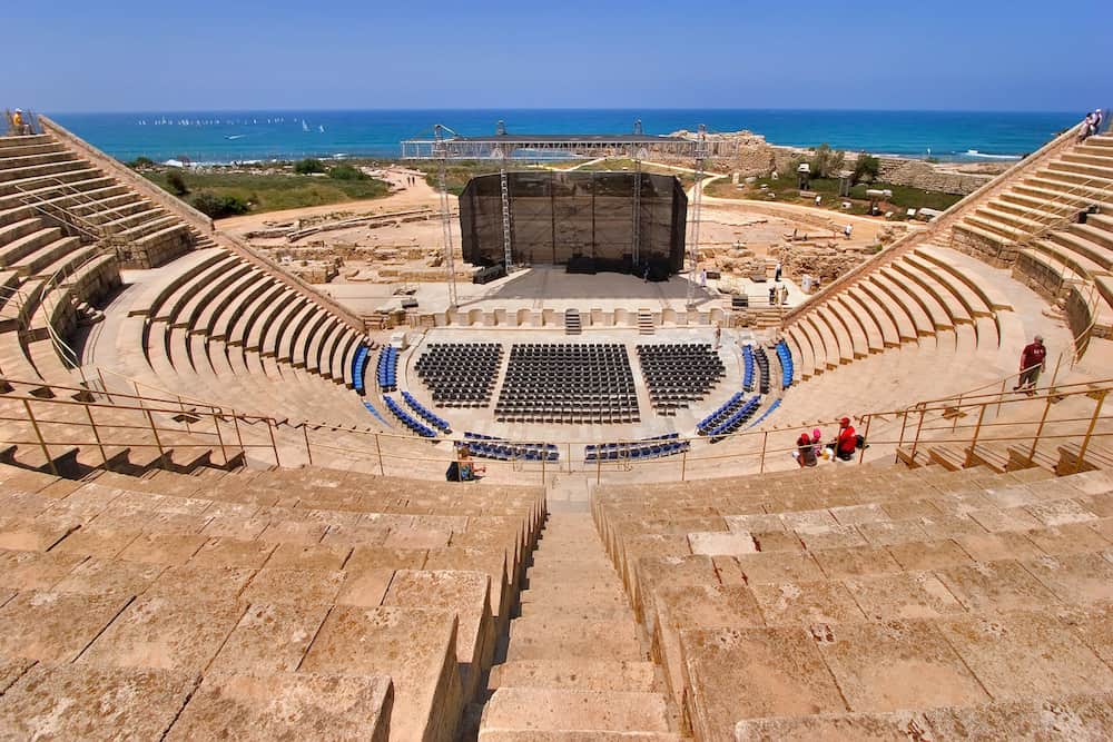 People sit in an amphitheater with a view of the water in the distance.