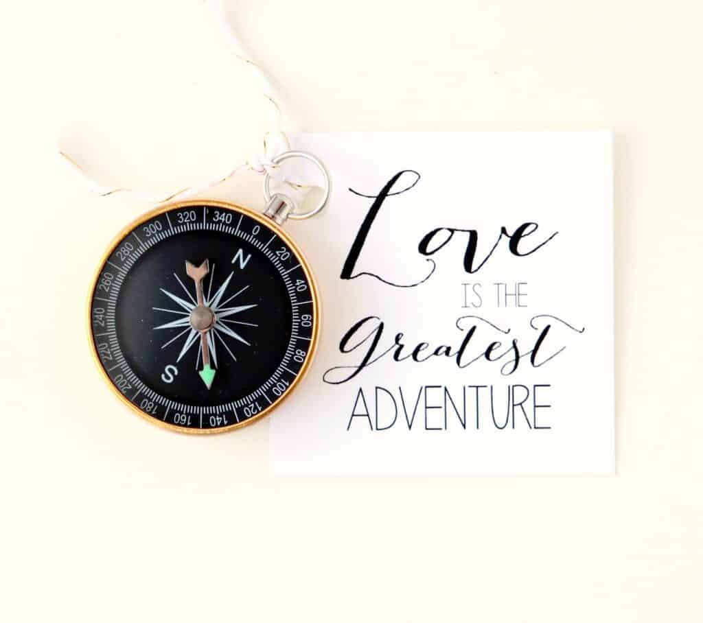 A compass is next to calligraphy that says love is the greatest adventure.