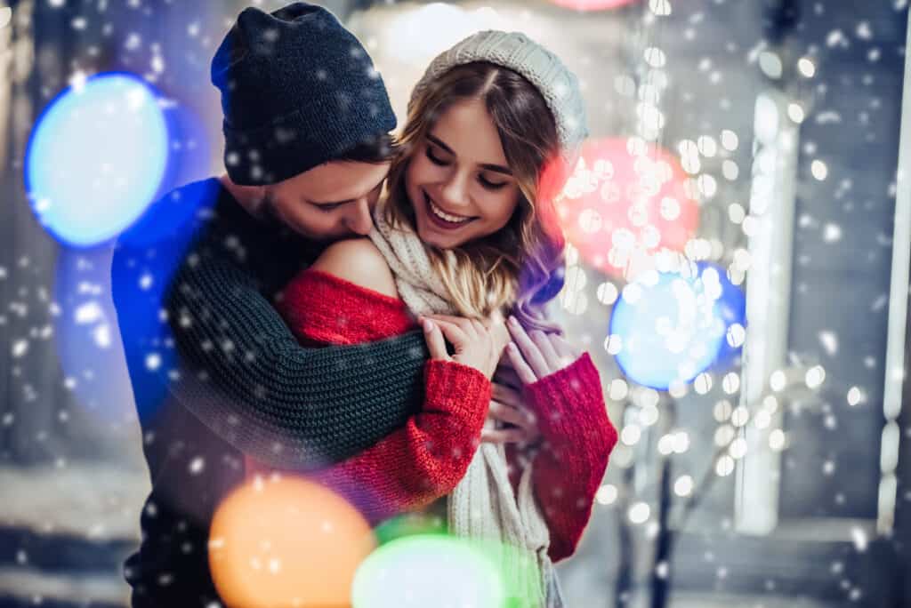 A couple cuddles outdoors in winter clothing.