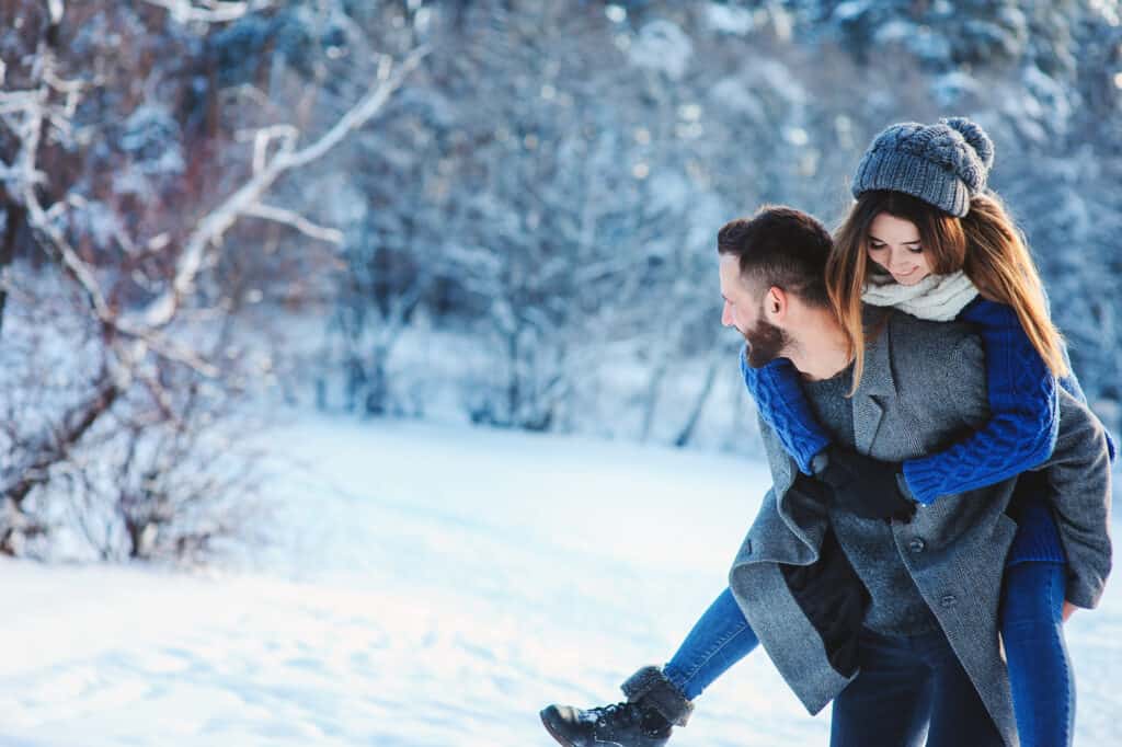 couple walking in snow man giving woman a piggy back