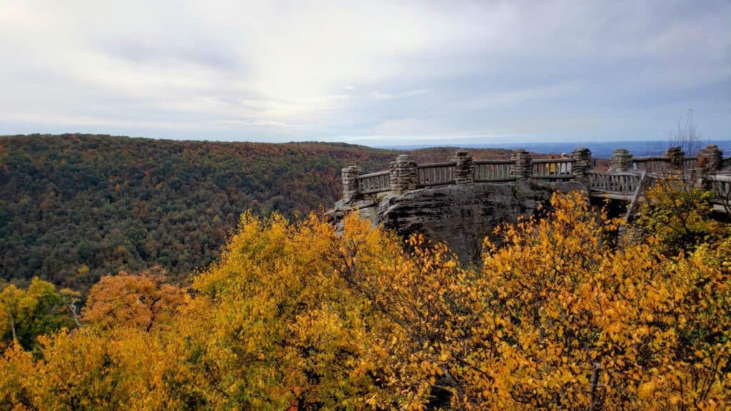 A viewpoint with a fence around it looks out to mountains in the fall.