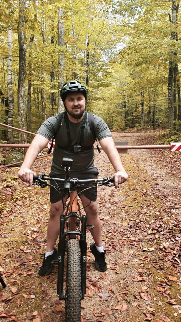 A man smiles riding a bike in the forest in fall.