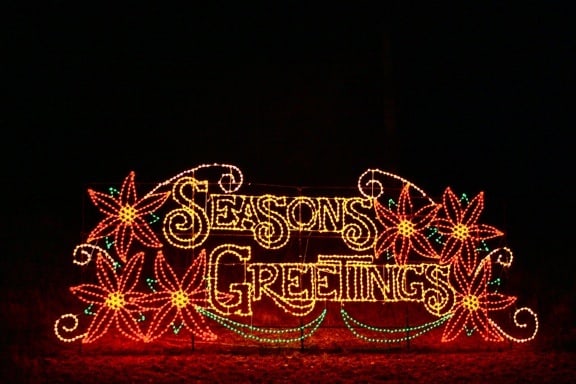 A lit-up sign outdoors at night that says \"Seasons Greetings.\"