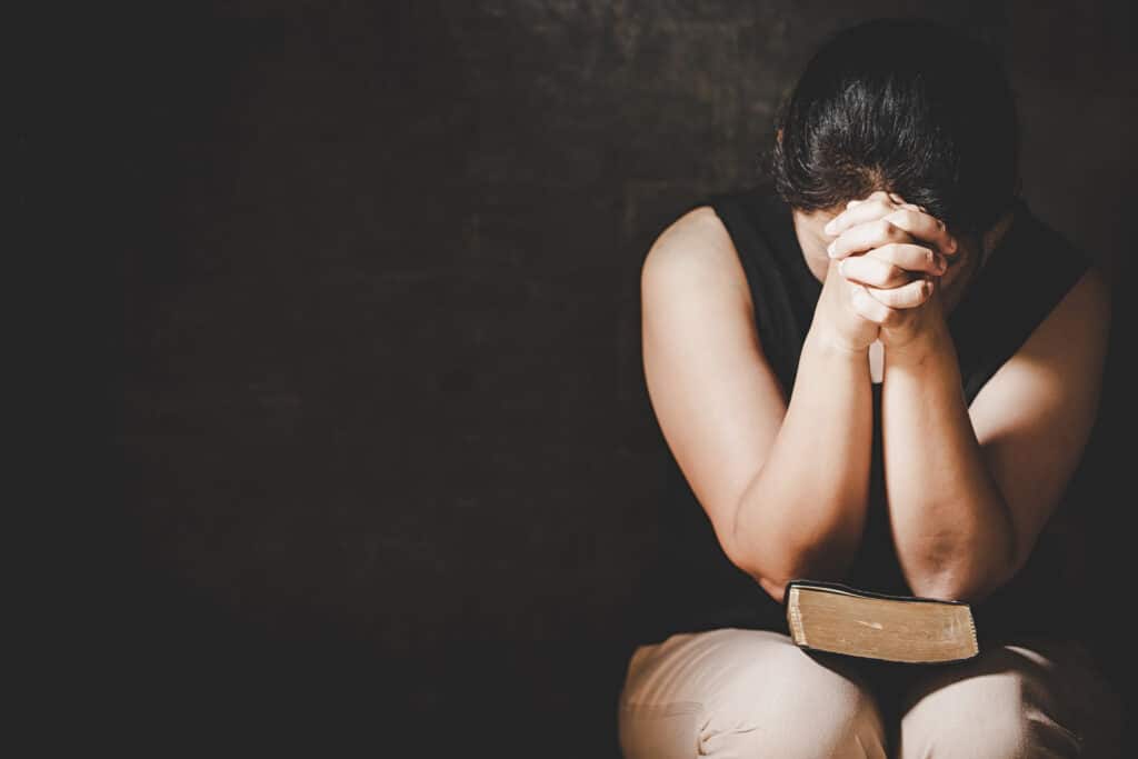 A woman is praying with her head leaned against her hands over the Bible.