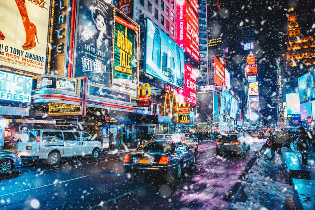 A busy street in New York City with large billboards as snow falls.