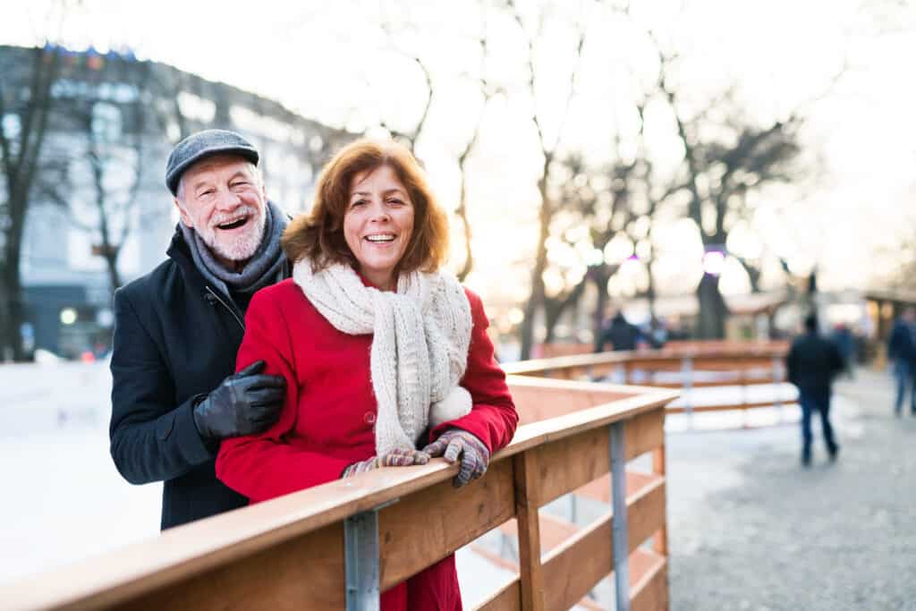 A man and woman smile outdoors in winter clothing.
