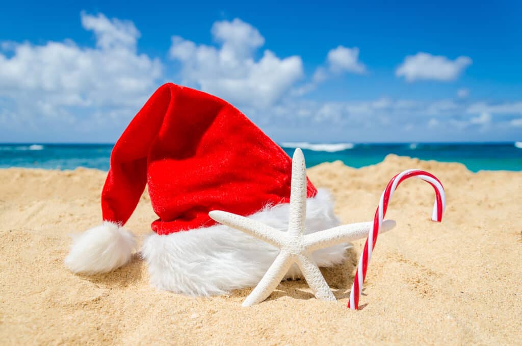 A Santa hat sits on the beach next to a starfish and candy cane.