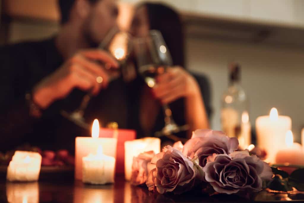 Roses and candles sit on a table while a man and woman cheers in the background.