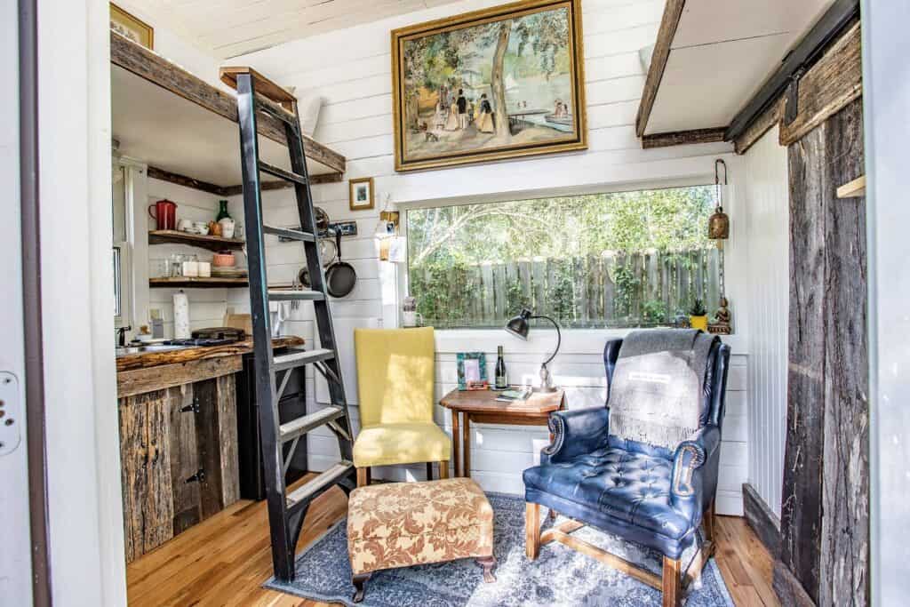 An eclectic room is filled with a lofted bed, kitchen, area, and seating area.