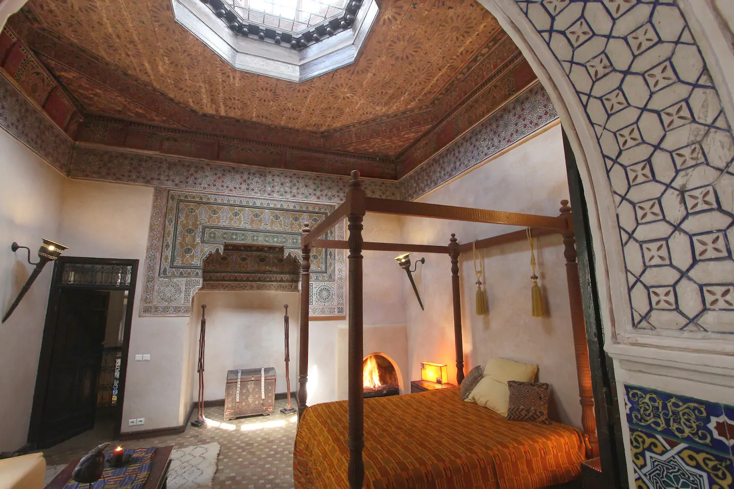 Interior of a room with a wooden framed bed. The ceiling has a big window in it, letting in lots of light.