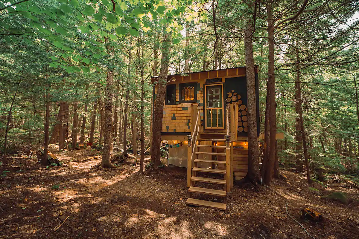 A cabin in the woods has stairs leading up to its front door.